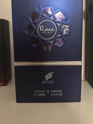 Afnan Rare Reef Extrait de Parfum - Snygg och elegant parfymflaska från Afnan, Rare Reef Extrait de Parfum. Flaskan är djupblå med silverdetaljer och har en modern, rund form. Volymen är 100 ml. Perfekt för dig som vill ha en unik och lyxig doft i samlingen.