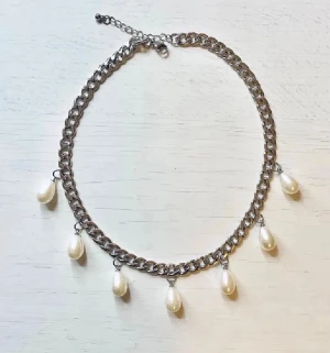 Kedjehalsband med droppformade pärlor - Snyggt halsband i silverfärgad metall med droppformade vita pärlor som hänger längs kedjan. Perfekt för att ge en trendig touch till din outfit. Justerbar längd med karbinlås. Passar dig som gillar statement-smycken.