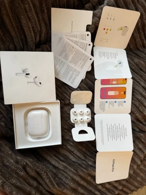 Apple AirPods Pro 2ND generation  - Säljer ett par vita Apple AirPods Pro med laddningsetui och extra silikonpluggar. Hörlurarna har en stilren och kompakt design i plast och levereras med originalförpackning och manualer. Perfekta för dig som vill ha grymt ljud och smidig anslutning till din iPhone.