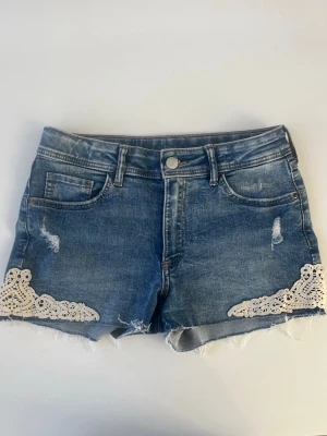 Blå jeansshorts med spets - Säljer ett par blå jeansshorts från hm med vita spetsdetaljer på sidorna. De är i storlek 164 men skulle säga att de även passar xs och s. De är i mycket bra skick och använda fåtal gånger.