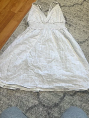 Vit omlottklänning med v-ringning - Säljer en vit kortklänning med omlott-design och v-ringad fram. Klänningen har smala axelband och ett elastiskt parti i midjan som ger en snygg passform. Perfekt för varma dagar och sommarens alla tillfällen.