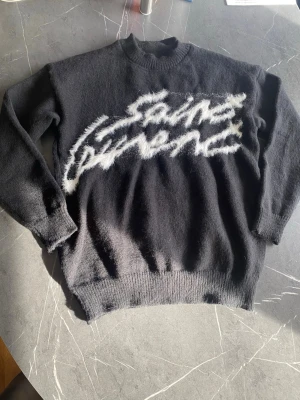 Svart stickad tröja – fluffig logga – strl M – streetwear - Säljer en svart stickad tröja i storlek M med stor text framtill i fluffigt/mohair-liknande material – riktigt clean och trendig streetwear-look.  Detaljer: 	•	Storlek: M 	•	Färg: svart 	•	Stickad / mjuk kvalitet 	•	Fluffig broderad text framtill 	•	Ribbad mudd vid hals, ärmar och nederkant  Skick: bra begagnat skick (se bilder) Passar perfekt till höst/vinter eller som oversized fit beroende på hur du vill bära den.  Säljs enligt bilder. Hör av dig vid frågor!  Kan skickas eller mötas 