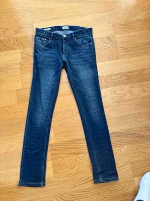 Mörkblå slim fit jeans - Snygga mörkblå slim fit jeans med klassisk femficksdesign och subtila slitningar framtill. Jeansen har normal midja och raka ben. Perfekta till vardagslooken och passar till det mesta. Materialet är mjukt och stretchigt för extra komfort.