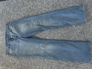 Ljusblå raka jeans med knappar - Säljer ett par ljusblå jeans med rak passform och knappgylf. Jeansen har klassisk femficksdesign och är tillverkade i denim. Perfekta för en avslappnad och trendig look.