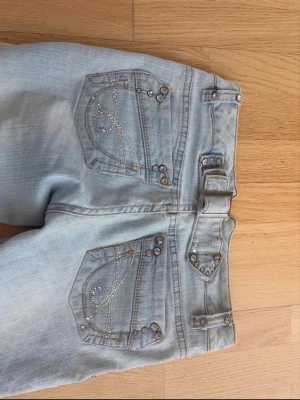 Ljusblå jeans med fina detaljer  - Jättefina low waist bootcut jeans med fina detaljer på fickorna och med justerbar midja. Vet tyvärr inte vilket märke det är och det står ingen storlek men skulle säga att det passar som xs. Det finns en liten fläck på ena benet som inte syns på kameran💕