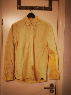 Gul långärmad skjorta från Morris - Säljer en stilren gul skjorta med lång ärm och klassisk krage. Skjortan har vita knappar och är gjord i ett lätt bomullstyg som känns skönt mot huden. Perfekt för dig som vill ha en färgklick i garderoben.