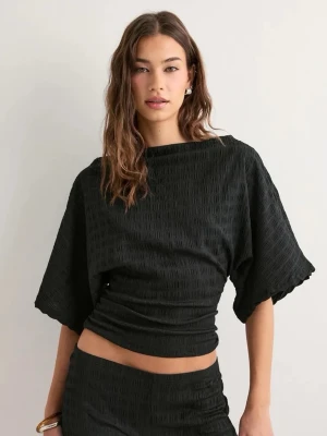 Svart topp med vida ärmar - Säljer en svart topp med lös passform och vida, korta ärmar. Toppen har en lätt struktur i tyget och en något croppad modell som ger en modern look. Perfekt att styla med höga byxor eller kjol. Lappen kvar!