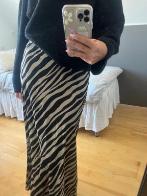 Zebramönstrad långkjol  - Säljer en snygg långkjol med zebramönster i svart och beige. Kjolen har en rak och ganska simpel passform med resår i midjan baktill. Jag är ca 174 cm lång som jämförelse. Kjolen är endast använd en gång🙌🏻🌟