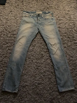 Ljusblå jeans från Replay - Säljer ett par ljusblå jeans från Replay med slitna detaljer och klassisk femficksdesign. Jeansen har raka ben och är tillverkade i bomull med en skön passform. Perfekta för dig som gillar en avslappnad och trendig look. W33 L34. Aldrig använts men klippte bort lappen. 
