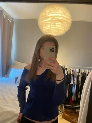 Mörkblå off shoulder tröja - En snygg mörkblå tröja med off shoulder-design och V-ringning. Tröjan har långa ärmar och en avslappnad passform som ger en cool och trendig look. Perfekt för dig som gillar att sticka ut och vill ha något bekvämt men stilrent. Marinull 