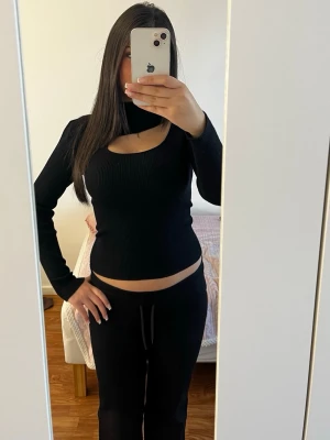 Svart ribbad topp med cut-out - Trendig svart långärmad topp med ribbad struktur och snygg cut-out detalj vid halsen. Toppens material ser ut att vara stretchigt och bekvämt, perfekt för att skapa en cool look. Passar dig som gillar stilrena och moderna plagg.