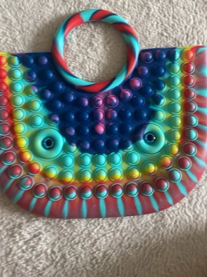 Pop it väska  - En pop it väska med ögon, multiföretag. Den är stor och man kan förvara saker i den. Perfekt för att ha kul men också användbart!