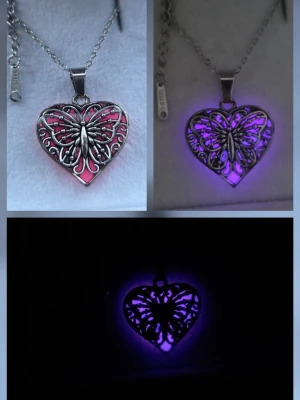Glow hjärtformat halsband med fjäril - Unikt halsband med ett hjärtformat hänge i silverfärgad metall. Hänget har ett detaljerat fjärilsmotiv och byter färg från rosa i dagsljus till lila i mörker. Vanligt dagsljus aktiverar effekten i hänget och det börjar därför att lysa/ ge ett lila sken i mörker som kan vara i flera timmar. Perfekt statement-piece för dig som gillar smycken med coola effekter och snygg design. Kedjan är 45 cm i rostfritt stål. Handgjort halsband. Tål vatten och missfärgas inte. Lång livslängd.