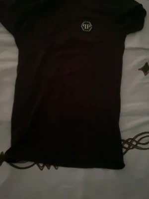 Svart t-shirt från Philipp Plein - Säljer en svart t-shirt från Philipp Plein med diskret logotyp på bröstet. T-shirten har klassisk passform och korta ärmar, perfekt för dig som gillar stilrena plagg med designer-touch. Materialet känns mjukt och bekvämt mot huden.