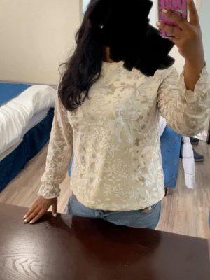 Vit spetsblus med blommönster - Säljer en vit blus i genombruten spets med blommönster. Blusen har långärmade ärmar med lätt puff och resår vid ärmslut. Perfekt för dig som gillar romantisk och feminin stil. Materialet är tunt och transparent, vilket ger en luftig känsla.