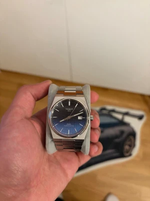 Tissot PRX blå klocka i stål - Snygg Tissot PRX klocka med blå urtavla och datumvisning. Klockan har ett stilrent armband i rostfritt stål och en klassisk rund boett. Perfekt accessoar för dig som gillar en modern och tidlös look. FULL SET / KVITTO