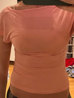 Ljusrosa topp med öppen rygg - Säljer en ljusrosa croppad topp med korta ärmar och öppen rygg. Toppen har en tight passform och är tillverkad i ett mjukt syntetmaterial. Perfekt för dig som gillar trendiga och unika plagg.