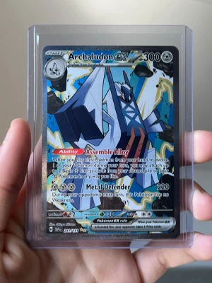 Archaludon EX Pokémonkort - Säljer ett Archaludon EX samlarkort från Pokémon TCG. Kortet har en färgstark design med blå, vit och gul bakgrund och metallic-effekter. Det ligger i ett genomskinligt plastskydd. Perfekt för dig som vill utöka din samling eller spela Pokémonkort. Väldigt fint och vra för samlare