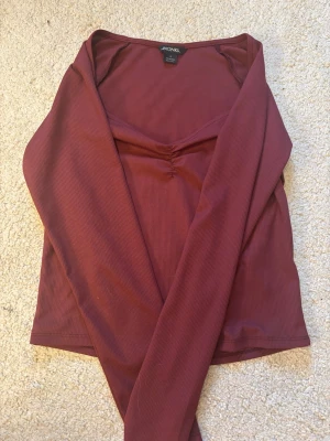 Vinröd topp från Monki - Trendig vinröd långärmad topp från Monki. Den är perfekt att styla med både jeans och kjol.