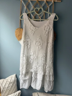 Vit broderad sommarklänning - Luftig vit klänning med broderade blommor och volangdetaljer. Ärmlös modell med rund halsringning och dubbla lager i nederdelen för extra flow. Perfekt för varma dagar och har en romantisk känsla. Storlek i S men passar även M🩷
