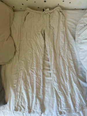 Beige linnebyxor från H&M - Säljer ett par beige linnebyxor från H&M med raka ben och dragsko i midjan. Byxorna har sidofickor och är tillverkade i ett lätt och luftigt linnematerial som är perfekt för varma dagar. Enkel och stilren design som är lätt att matcha.