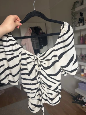 Zebramönstrad omlott topp med snörning - Säljer en vit och svart zebramönstrad topp med snörning framtill och puffiga korta ärmar. Toppen är i xs och är lite  croppad. perfekt till fest men säljer pågrund av att den inte passar längre❤️❤️😇😇😇