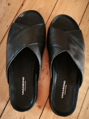 Svarta Vagabond lädersandaler strl 38 - Snygga svarta sandaler från Vagabond i äkta läder med breda korslagda remmar och platt sula. Storlek 38, endast testade vid två tillfällen. 