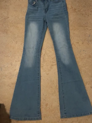 Blå utsvängda jeans med hög midja - Säljer ett par ljusblå jeans med utsvängda ben och hög midja. Jeansen har klassisk femficksdesign och är tillverkade i denim med lätt tvättade partier framtill. Perfekta för en trendig och avslappnad look.