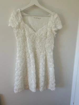 Vit blommig kortklänning från Ida Sjöstedt - Säljer min älskade studentklänning… Superfin vit kortklänning från Ida Sjöstedt med blommiga 3D-rosor över hela klänningen. Klänningen har korta ärmar och v-ringad fram. Den har inga defekter, skriv för fler bilder!!