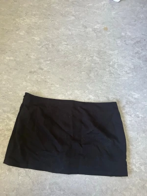 Svart kortkjol  - Säljer min svart mini kjol då den inte används längre. Den har inbyggda short och dragkedja på sidan. 