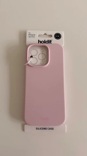 Ljusrosa silikonskal Holdit iPhone 16 Pro - HELT NYTT OCH OÖPPNAT ljusrosa mobilskal från Holdit, gjort i mjukt silikon och designat för iPhone 16 Pro. Skalet har en stilren och slät yta med rundade hörn och extra skydd runt kameran. Perfekt för dig som vill ha ett trendigt och minimalistiskt skydd till mobilen. 