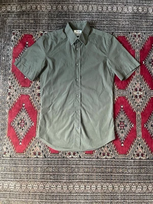 Grön kortärmad skjorta Acne Studios - Kortärmad skjorta från Acne Studios, modell Otis SH Pop.  Färg: olivgrön Storlek: 46 (passar S) Passform: slim fit  Bra skick. Liten öppning i sömmen under armen (se bild, lätt att fixa).  Nypris ca 1400 kr.  Perfekt till vår/sommar.