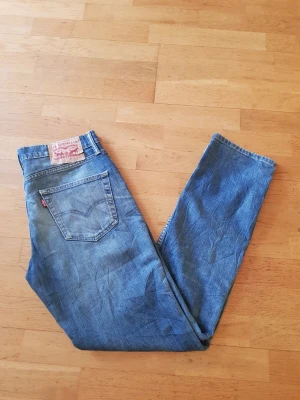 Levi's 511 blå jeans - Säljer ett par klassiska blå Levi's 511 jeans med rak passform och fem fickor. Jeansen har den ikoniska röda Levi's-lappen på bakfickan och patch i läder bak i midjan. Tillverkade i slitstarkt denimtyg, perfekta för en avslappnad och tidlös stil.