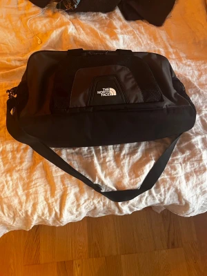 Svart duffelväska från The North Face - Snygg och rymlig svart duffelväska från The North Face med justerbar axelrem och bärhandtag. Väskan har ett stort huvudfack och mesh-detaljer på sidorna. Perfekt för gymmet eller resan, tillverkad i slitstarkt material. I mycket bra skick då den köptes 2025. 