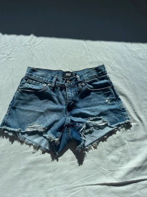 Jeansshorts  - Säljer ett par blå jeansshorts med fransig kant och slitna detaljer.