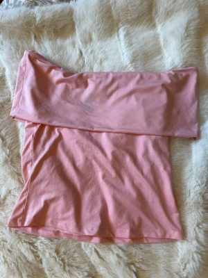 Ljusrosa axelbandslös topp - Säljer en ljusrosa axelbandslös tubtopp i mjuk bomull. Toppen har en bred kant upptill som ger en snygg offshoulder-look och är perfekt för varma dagar. Köpte second hand men har själv aldrig använt den. Finns en liten defekt, se bild. 