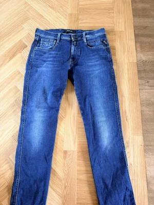 Blå raka jeans från Replay - Säljer ett par klassiska blå jeans från Replay med raka ben och fem fickor. Jeansen har snygga slitningar och kontrastsömmar, samt Replay-logga på bakfickan. Tillverkade i mjukt denimtyg som sitter skönt hela dagen.