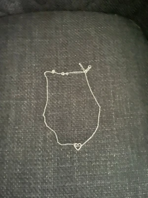 Silverfärgat halsband med hjärthänge - Snyggt och stilrent halsband i silverfärg med ett litet hjärta som hänge. Kedjan är tunn och smidig, perfekt för att ge en subtil touch till din outfit. Hjärtat är öppet och minimalistiskt, vilket gör halsbandet lätt att matcha med andra smycken.