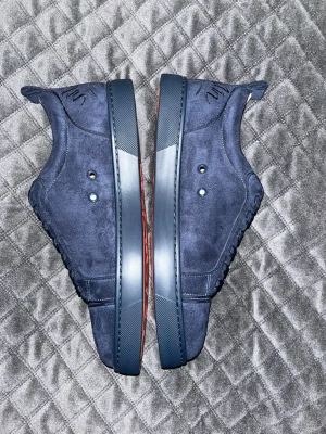 Mörkblåa sneakers från Christian Louboutin - Snygga mörkblå sneakers i mocka från Christian Louboutin akopi med klassisk låg siluett och matchande blå snörning. Skorna har diskreta detaljer och den ikoniska röda sulan som sticker ut. Perfekta för dig som vill ha något exklusivt och stilrent.