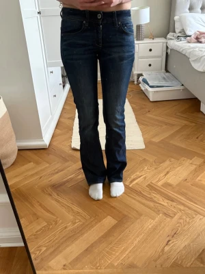 Mörkblå bootcut jeans - Snygga mörkblå bootcut jeans med klassisk femficksmodell och låg midja. Jeansen har kontrastsömmar och en liten läderpatch bak i midjan. Perfekta till sneakers eller boots för en avslappnad look.