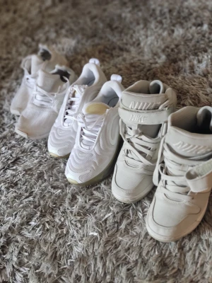 Tre par vita sneakers från Nike - Säljer tre par snygga vita sneakers från Nike. Ett par har högre skaft och kardborreband, de andra två är låga modeller med klassisk snörning. Alla är i vitt med olika detaljer och materialmix, perfekta för dig som gillar stilrena och sportiga skor.