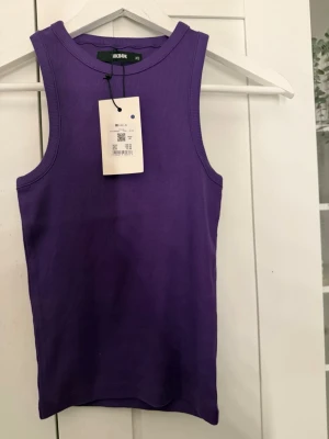 Lila ribbad linnetopp från BikBok - Säljer en snygg lila ribbad linnetopp från BikBok i storlek XS. Toppen är ärmlös och har en klassisk rund halsringning. Perfekt att styla med jeans eller kjol för en trendig look.