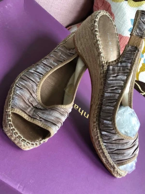 Beiga kilklackade espadrilles från Nome - Säljer ett par beiga espadrilles med kilklack från Nanon. Skorna har öppen tå, rynkad textil med lyster  på ovandelen och klassisk flätad sula i jute. Slingback-remmen ger en skön och somrig känsla. Perfekta till jeans eller klänning!