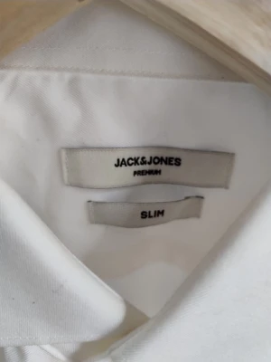 Vit slim fit skjorta Jack & Jones - Klassisk vit skjorta från Jack & Jones Premium i slim fit-modell. Skjortan har lång ärm, knäppning framtill och en stilren krage. Perfekt för dig som gillar en enkel och clean look. Materialet är mjukt och följsamt, troligen bomull.