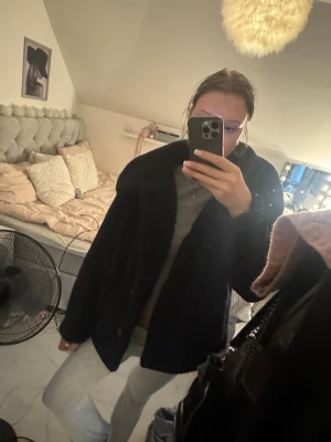Svart teddyjacka med stora knappar - Mysig svart teddyjacka med stora rutmönstrade knappar och två framfickor. Jackan har en oversized passform och är gjord i fluffigt teddy-material som håller dig varm. Perfekt för kalla dagar och ger en trendig look till din outfit.