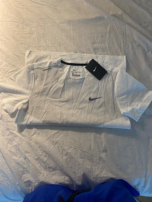 Vit Nike t-shirt med logga - Snygg vit t-shirt från Nike med diskret rutmönster framtill och svart Nike-logga på bröstet. Klassisk passform och rund halsringning. Perfekt till träning eller chill. Tillverkad i mjuk bomull för skön känsla.