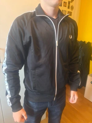 Svart Fred Perry zip-tröja - Säljer en svart zip-tröja från Fred Perry med vit dragkedja och logga på bröstet. Nypris 1500 kr! Priset går att diskuteras👊
