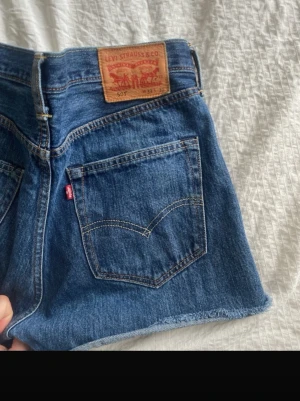 Levi's blå jeansshorts hög midja - Klassiska blå jeansshorts från Levi's med hög midja och rå kant nertill. Shortsen har fem fickor, knappgylf och den ikoniska läderlappen bak. Perfekta till sommaren och ger en avslappnad vintagekänsla.Vintage Levis 501s jeansshorts w33 L30 Midja: 42cm ish   fairy fairycore 2000s 00s gorset top mini britney spears model of duty old money lana del rey archive subversive basics bratz i am gia morgan twilight goth mallgoth alt alternative mesh top fishnet miss sixty bimbo xoxo juicy couture paris hi