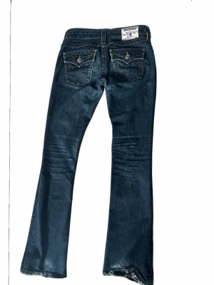 Vintage 2000s bootcut true religion  - Vintage true religion jeans som är super low waist storlek w25 midjemått:37cm  Innerbenslängd:82cm grenmått: 19cm Jeansen har blivit upptrampade och  tråden på fållen på ena sidan har gått upp, går enkelt och fixa men jag har inte orkat.