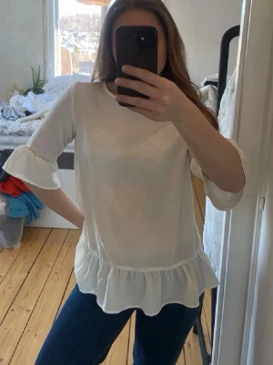 Vit blus med volangdetaljer 36  - Söt vit blus med volangkant nedtill och vid ärmslut. Blusen har rund halsringning och trekvartsärm med lätt puff. Materialet är tunt och luftigt, perfekt för en fräsch look. Passar till både jeans och kjol. Storlek 36 från Stockholm 💕